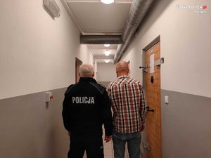 Zatrzymany mężczyzna tyłem z policjantem na korytarzu