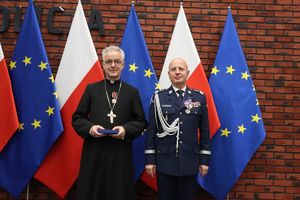 Komendant Główny Policji i ksiądz stoją na tle flag Polski i Unii Europejskiej