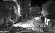 Czarno-białe zdjęcie z monitoringu. Ulica, na niej dwóch mężczyzn. Trzeci stoi na chodniku obok