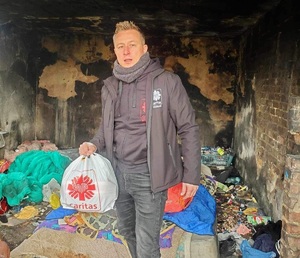wolontariusz stoi z reklamówką z darami dla bezdomnych, w tle pustostan