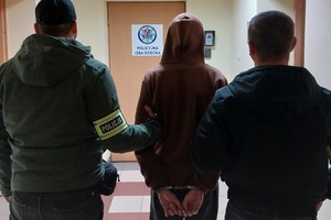 Dwóch policjantów prowadzi zatrzymanego przez korytarz
