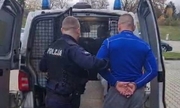 policjant wprowadzający do radiowozu zatrzymanego z założonymi kajdankami na ręce trzymane z tyłu