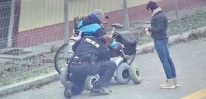 Zdjęcie z monitoringu. Policjanci pomagają mężczyźnie, któremu uszkodziło się koło przy wózku inwalidzkim. Obok stoi kobieta, która towarzyszyła mężczyźnie