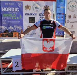 Asp. Marcin Brewczyński w stroju sportowym trzyma flagę Polski
