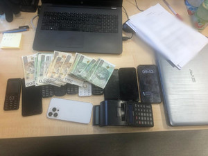 zabezpieczone przez policjantów przedmioty: laptop, telefony komórkowe, pieniądze, kalkulator leżące na blacie