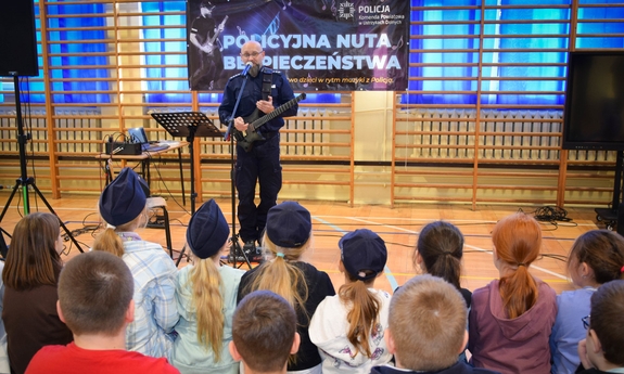 policjant podczas spotkania z dziećmi na sali gimnastycznej gra na gitarze
