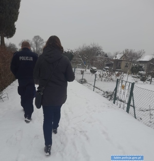Policjant i kobieta idą zaśnieżoną dróżką po działkach ogrodowych