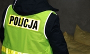 Zdjęcie kolorowe. Policjant odwrócony plecami w odblaskowej kamizelce