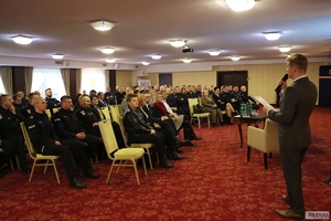 policjanci i inni goście konferencji siedzą w rzędach na krzesłach słuchając stojącego naprzeciwko nich mężczyzny