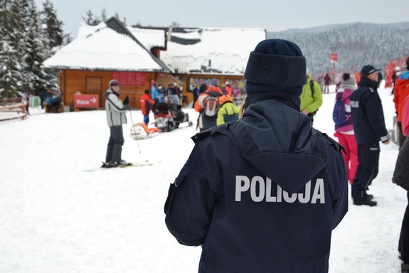 Policjantka odwrócona tyłem na tle stoku narciarskiego.