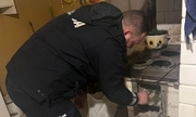 policjant w mieszkaniu mężczyzny przygotowuje piec do rozpalenia ognia