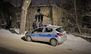 policjanci stoją przy radiowozie zaparkowanym przy opuszczonym budynku