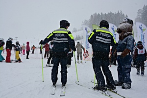 Policjanci na nartach odwróceni tyłem stoją obok policyjnej maskotki.