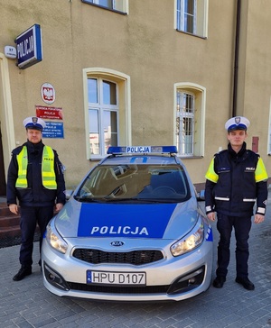 Dwóch policjantów stoi przy oznakowanym radiowozie