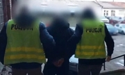 Dwaj policjanci w żółtych kamizelkach prowadza zatrzymanego