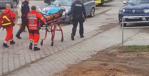 Ratownicy idący do pacjentki. Po bokach dwa źle zaparkowane samochody