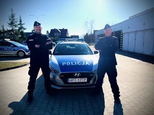 Dwaj policjanci st. sierż. Grzegorz Zieliński, st. post. Andrzej Ciechanowski stoją przy radiowozie policyjnym