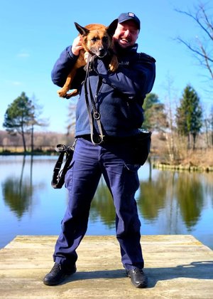 Policjant przewodnik trzyma na rękach swojego psa służbowego
