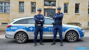 dwaj umundurowani policjanci stoją przy radiowozie