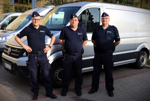 trzech umundurowanych policjantów stoi przy radiowozie