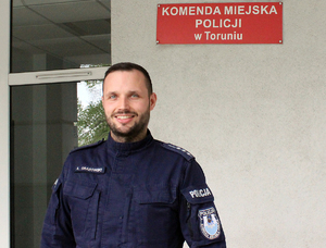 umundurowany policjant stoi pod budynkiem Komendy Miejskiej Policji w Toruniu
