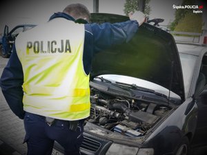 policjant w żółtej kamizelce z napisem Policja na plecach, zagląda pod maskę samochodu