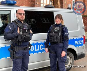 dwoje umundurowanych policjantów stoi przy furgonie policyjnym