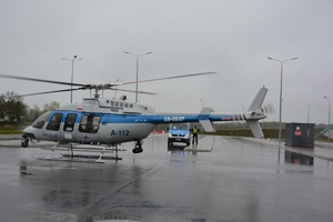 śmigłowiec policyjny na lądowisku, obok niego radiowóz i policjant