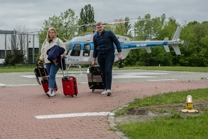 kobieta i mężczyzna na lądowisku z walizkami i pojemnikiem na narządy, w tle śmigłowiec