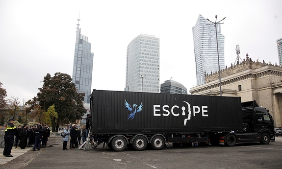 Escape van, przed którym gromadzą się ludzie. W tle miasto i zabudowania