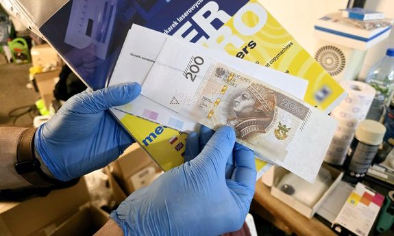 fałszywy banknot. po bokach od banknotu odstają białe końcówki