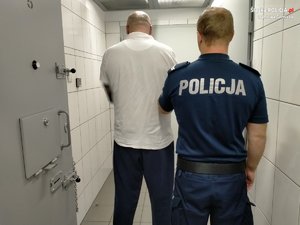 umundurowany policjant z zatrzymanym w korytarzu policyjnego aresztu, obaj stoją tyłem