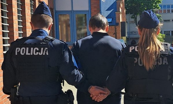 policjant i policjantka prowadzą zatrzymanego mężczyznę zakutego w kajdanki