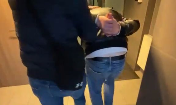 ubrany po cywilnemu policjant prowadzi zatrzymanego zakutego w kajdanki - widok z tyłu