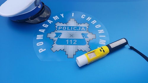 z lewej strony widoczna leżąca czapka policjanta ruchu drogowego, obok widać policyjną gwiazdę a wokół niej napis: Pomagamy i chronimy, z prawej strony zdjęcia widoczne jest Alcoblow - przyrząd do sprawdzania stanu trzeźwości kierujących