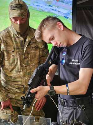 na zdjęciu umundurowany funkcjonariusz BOA prezentuje uczniowi klasy policyjnej broń służbową