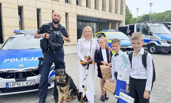 policjant z psem policyjnym i dziećmi. w tle radiowozy