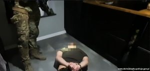 zatrzymany mężczyzna leży na podłodze. Nad nim stoją policjanci