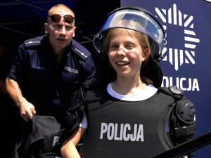 dziewczynka w hełmie i kamizelce policyjnej, z tyłu widać umundurowanego policjanta