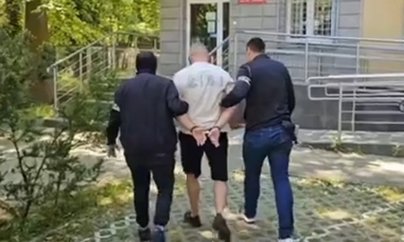 dwaj nieumundurowani policjanci prowadza zatrzymanego mężczynę zakutego w kajdanki