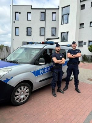 na zdjęciu dwóch umundurowanych policjantów stoi przy radiowozie