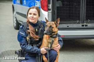 na zdjęciu umundurowana policjantka z psem służbowym, w tle radiowóz