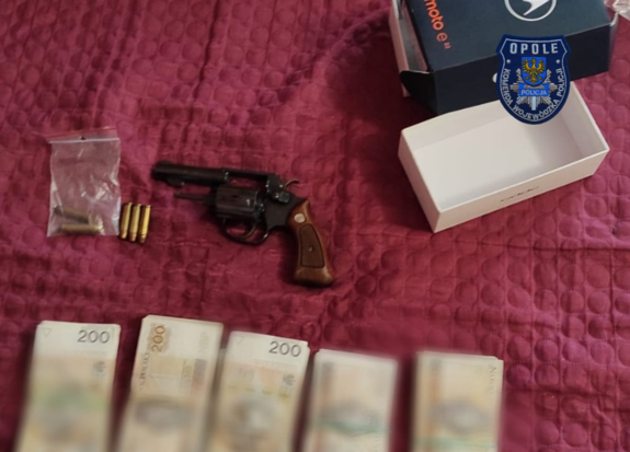 Zdjęcie przedstawia broń, obok leżą banknoty i amunicja
