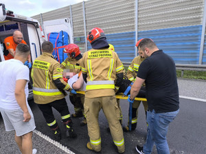 strażacy i mężczyzna pomagają przy wnoszeniu pacjenta do karetki