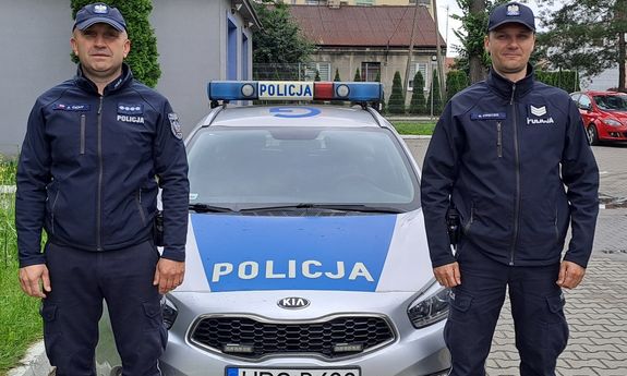dwóch policjantów stojących przy oznakowanym radiowozie