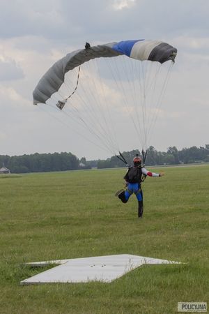 spadochroniarz ląduje, na ziemi strzałka wskazująca kierunek gdzie ląduje spadochroniarz