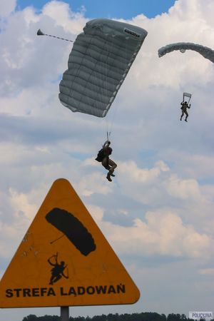spadochroniarze w tle, na pierwszym planie znak z napisem strefa lądowań