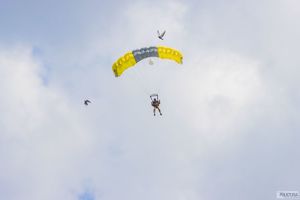 spadochroniarz z żółtym spadochronem leci na błękitnym niebie. Obok lecą dwa ptaki