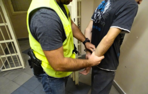 policjant w żółtej kamizelce zakłada na ręce zatrzymanego mężczyzny kajdanki