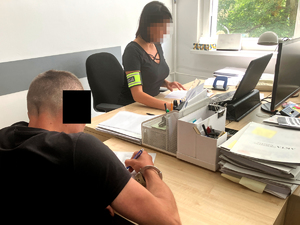zatrzymany mężczyzna siedzi przy biurku i podpisuje dokumenty, obok siedzi policjantka